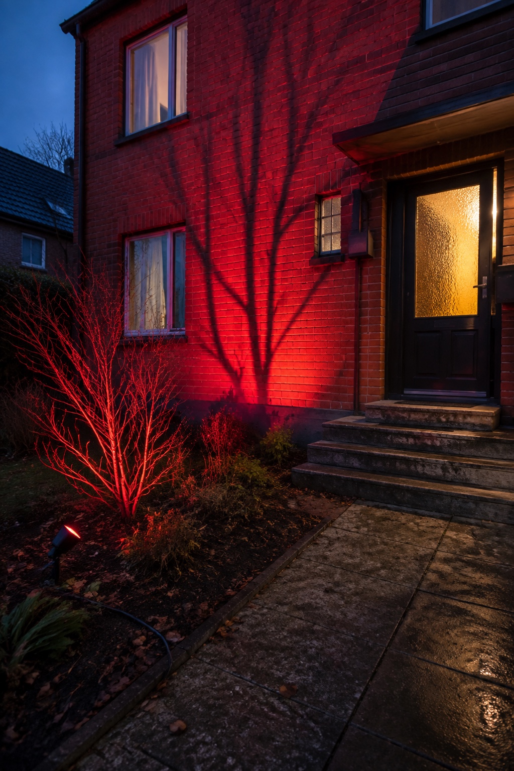 Rotes Licht wirft unheimliche Astschatten auf eine Backsteinfassade