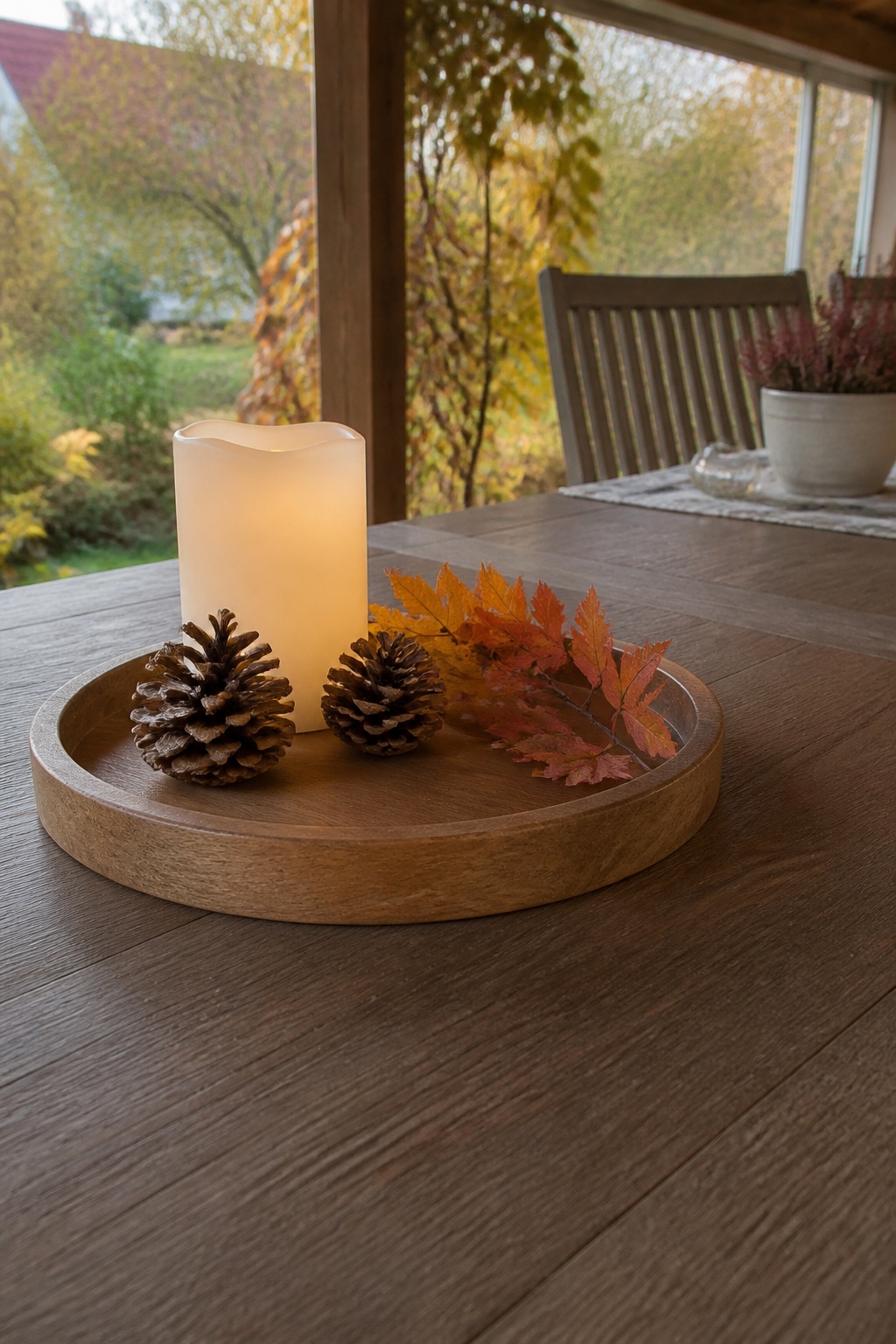 Rundes Holztablett mit LED-Kerzen, Zapfen und kleinem Zweig auf einem Terrassentisch