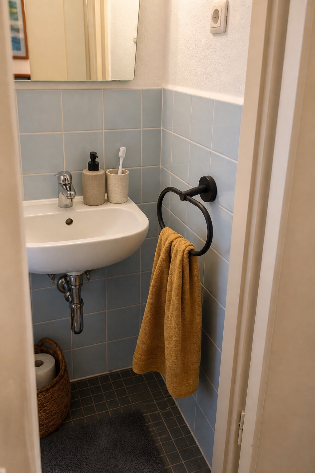 Schwarzer Handtuchring mit ockerfarbenem Handtuch neben kleinem Waschbecken