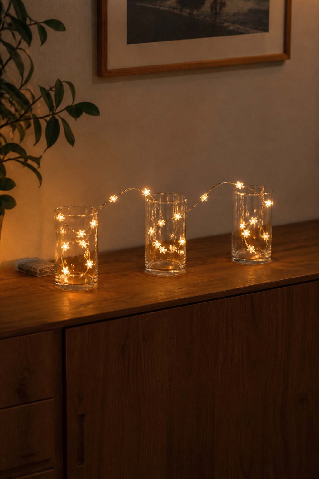 Drei Gläser in einer Reihe mit einer warmweißen Stern-Lichterkette auf einem Sideboard